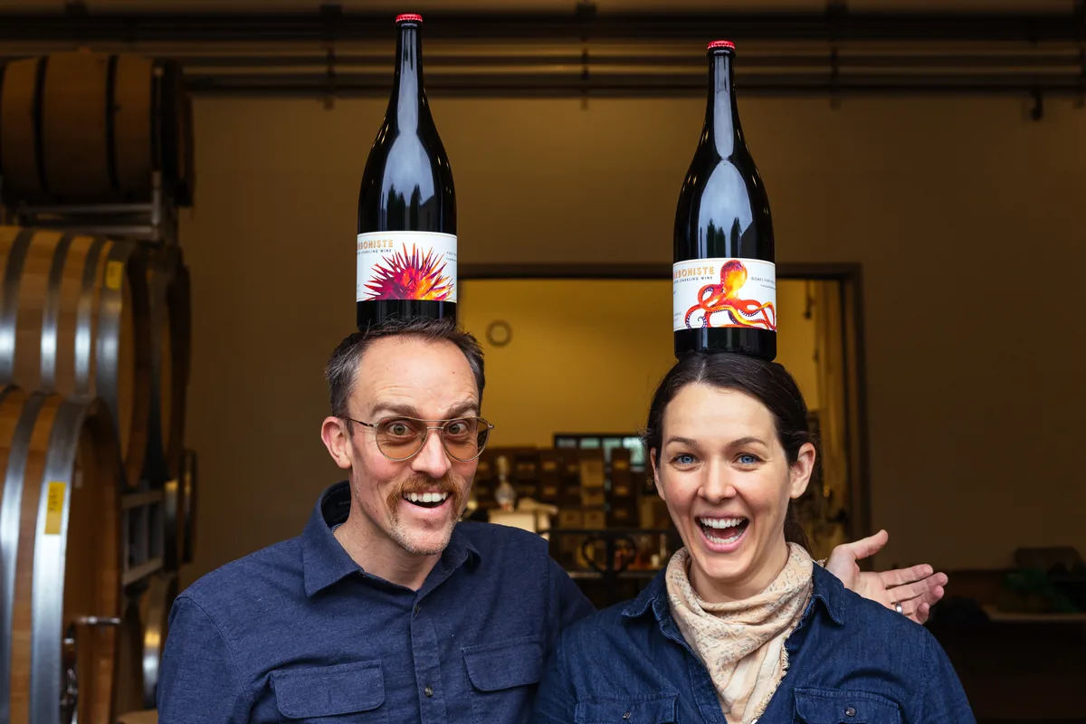Carboniste founders Dan and Jacqueline laughing at the winery door, each balancing a magnum of sparkling wine on their head